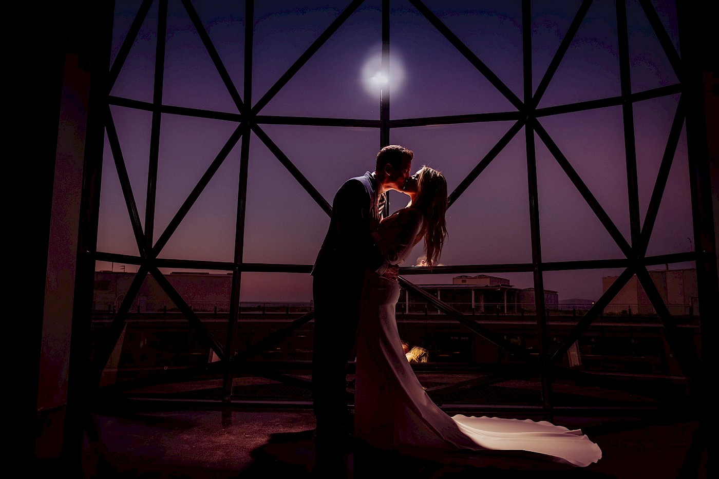 Romantic silhouette of newlyweds kissing - purple dusk sky - stunning window geometry background - Photo Greg Lumley